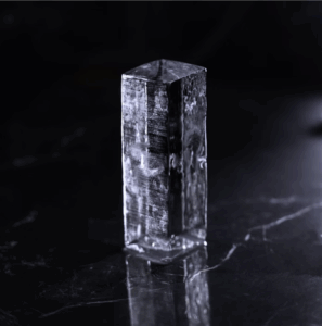 Un rectangle de glace transparent, lisse et posé sur une surface sombre avec son reflet visible.