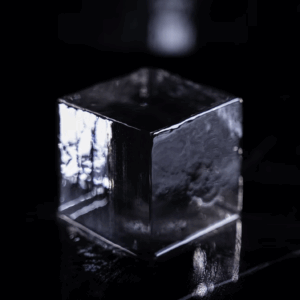 Un glaçon transparent et carré se tient debout sur une surface sombre et réfléchissante, où l'on distingue une légère réfraction de la lumière.