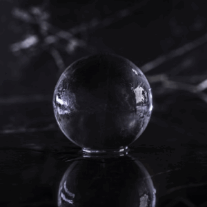 Boule de glace transparente sur une surface noire, avec reflets lumineux et ombres subtiles, créant une atmosphère mystique.