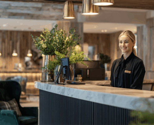 Hôtesse d’accueil souriante derrière un comptoir d’hôtel, représentant le professionnalisme et la qualité de service.